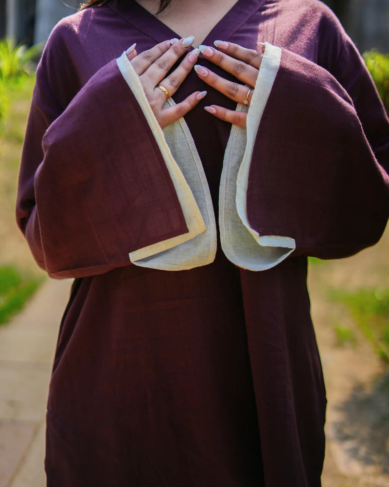 Person wearing a dark purple robe with white trim, standing outdoors.