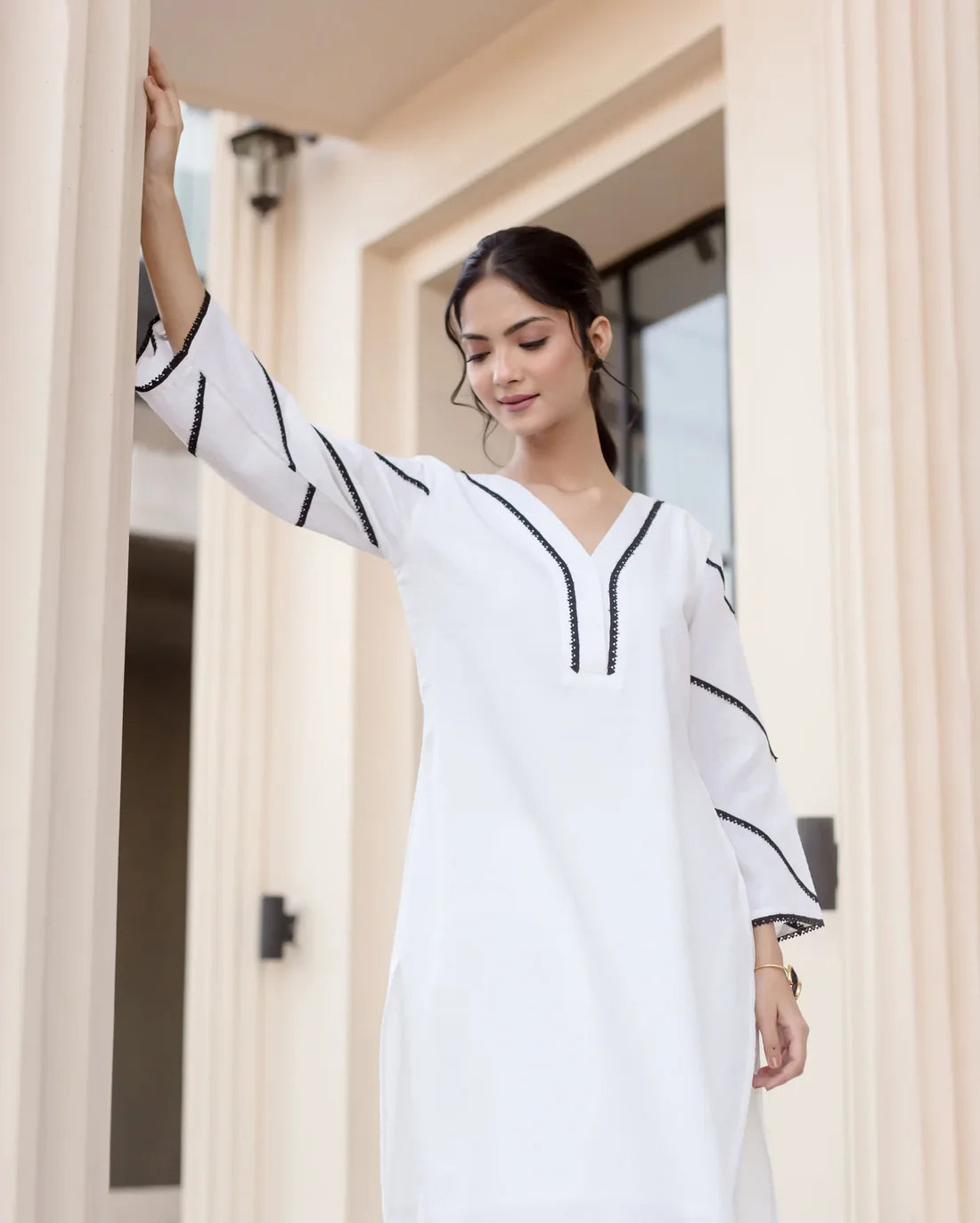 Woman wearing a white dress with black accents standing in a doorway.