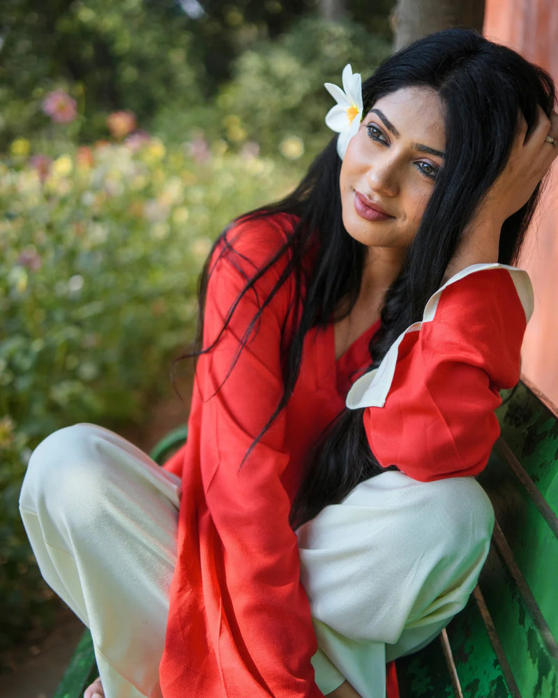 Woman in a red and white outfit with a flower in her hair, sitting outdoors.