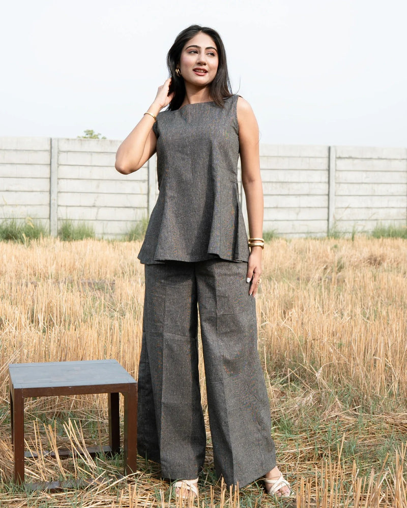 Woman wearing a gray sleeveless top and wide-leg pants standing in a field with a wooden table.
