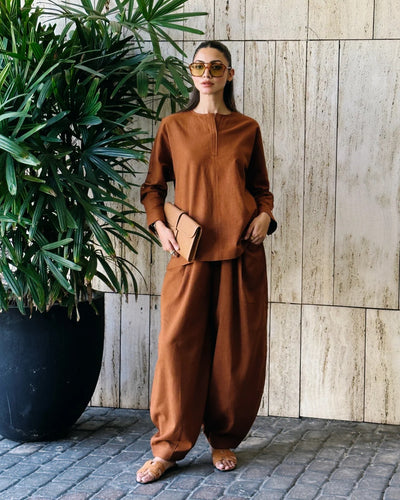 Woman in a brown outfit standing next to a potted plant against a wooden wall.