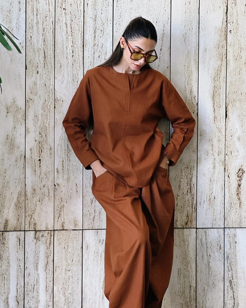 Person wearing a brown outfit against a wooden paneled wall.
