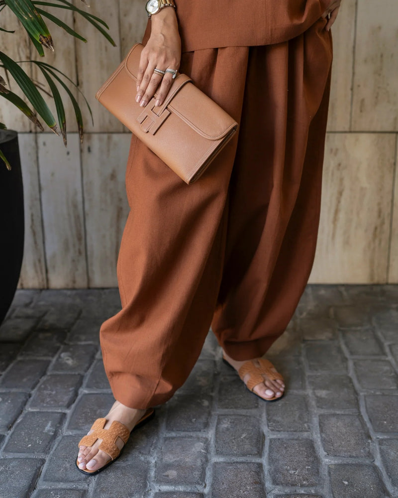 Person wearing brown pants and holding a matching clutch on a stone pavement.