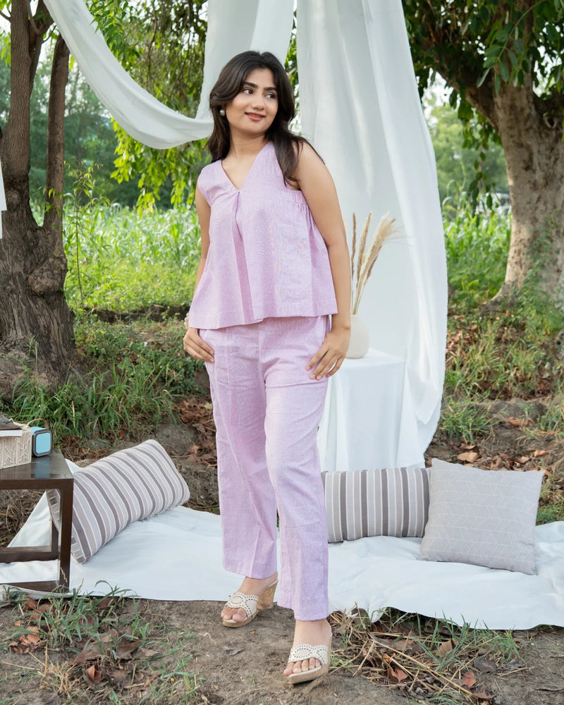 Woman in a light purple outfit standing in a garden setting with white curtains and pillows.