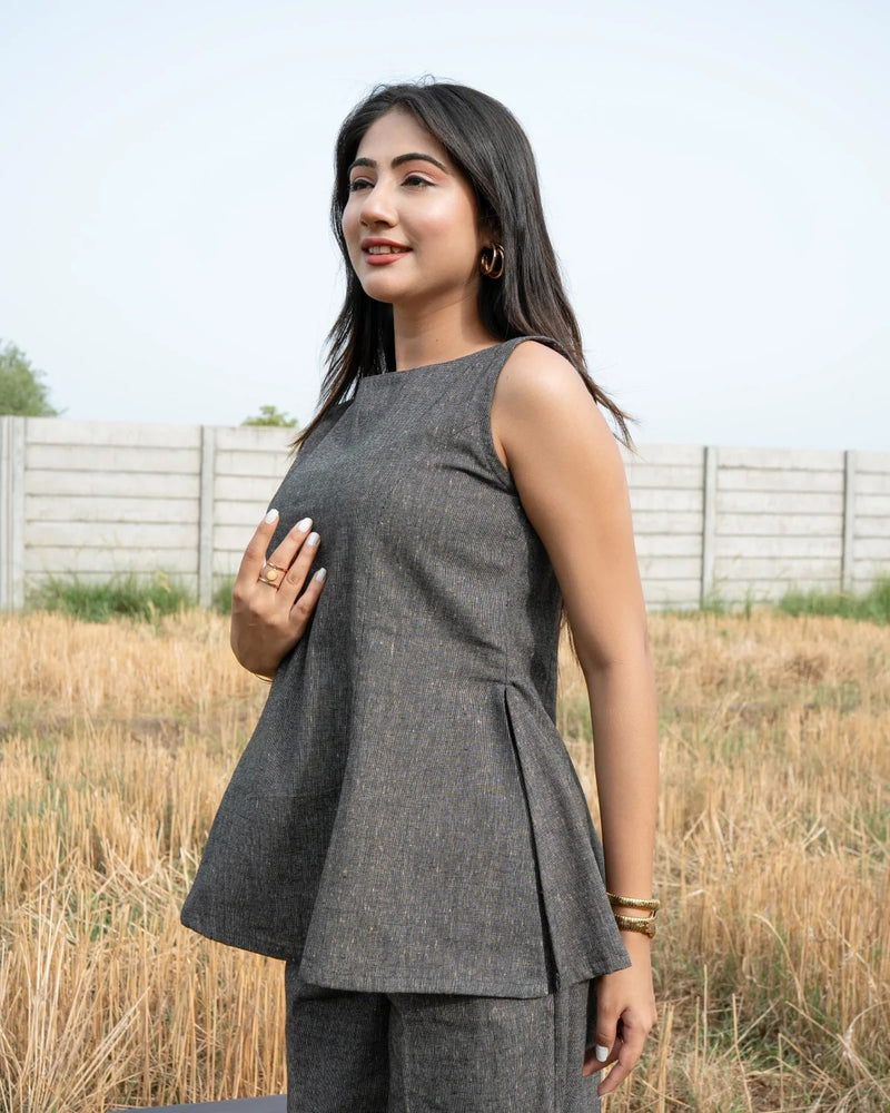 Woman wearing a gray sleeveless top and pants standing in an outdoor setting with a fence and grass.