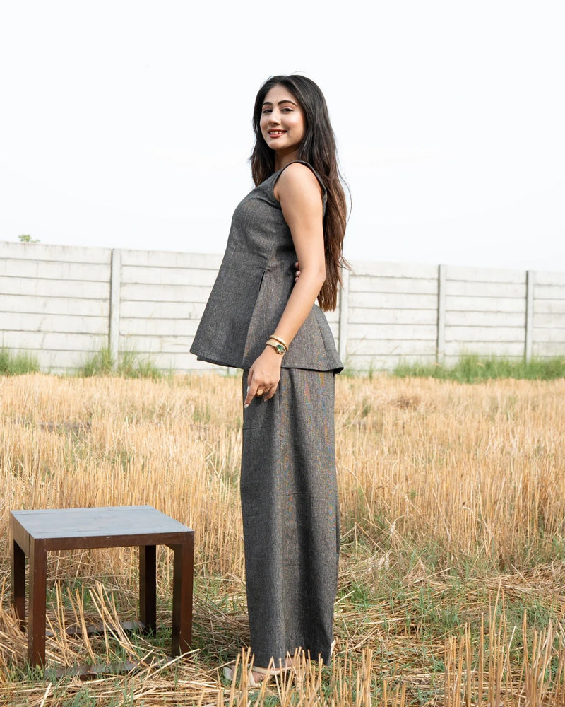 Woman in a gray outfit standing in a field with a wooden table nearby.