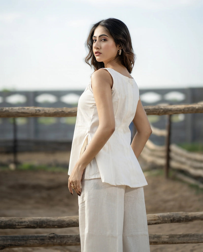 Woman wearing a white sleeveless top and light-colored pants standing outdoors with a blurred background