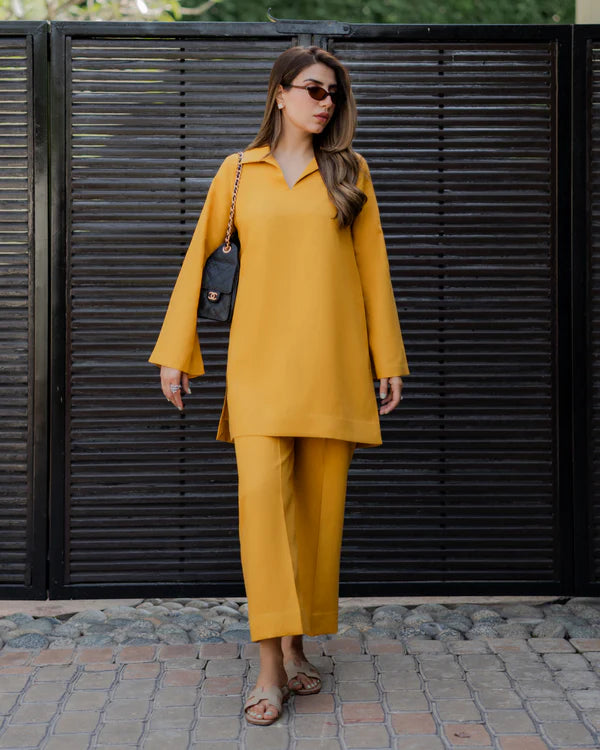 Woman in a mustard yellow outfit standing against a black metal gate.