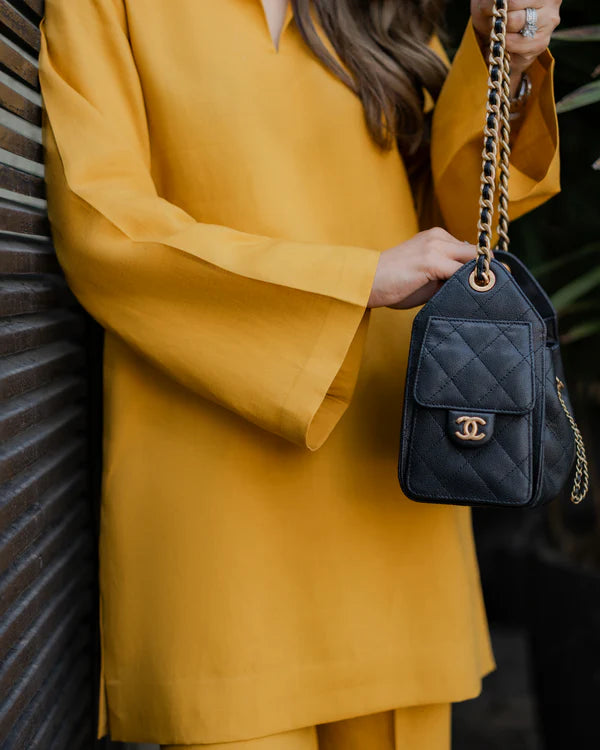 Person wearing a yellow outfit holding a black quilted handbag with a gold chain.