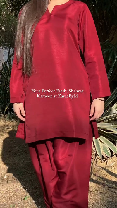Red Farshi Shalwar Kameez outfit with text overlay on a natural background