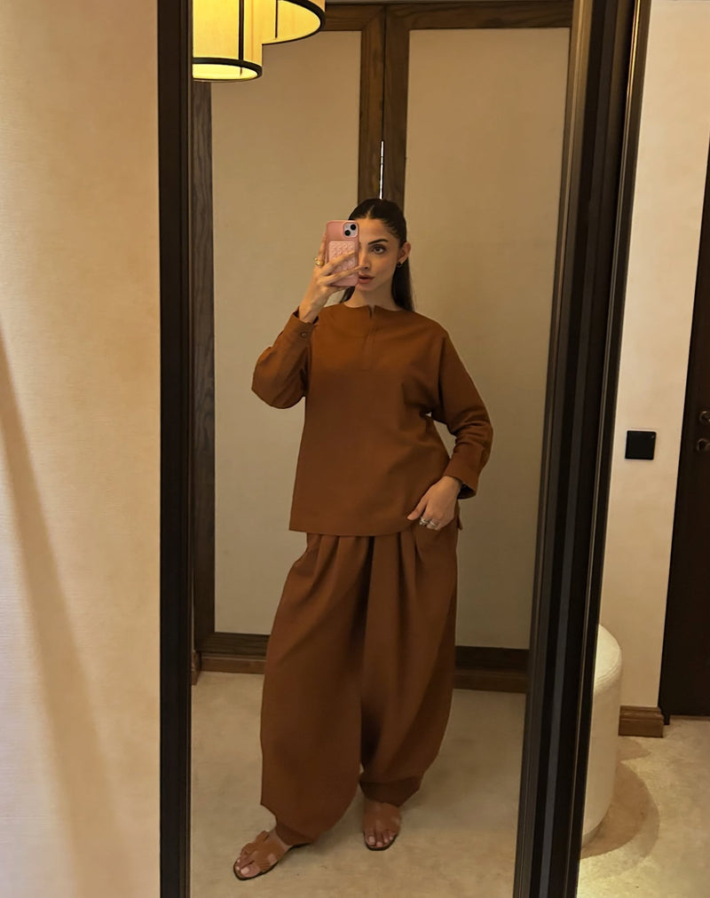 Person wearing a brown outfit taking a mirror selfie in a room.